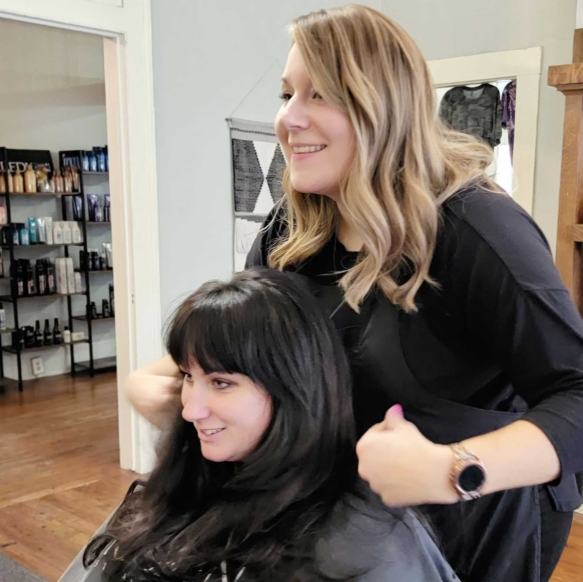 Hairdresser styling a client's hair in a salon with shelves of hair products in the background.