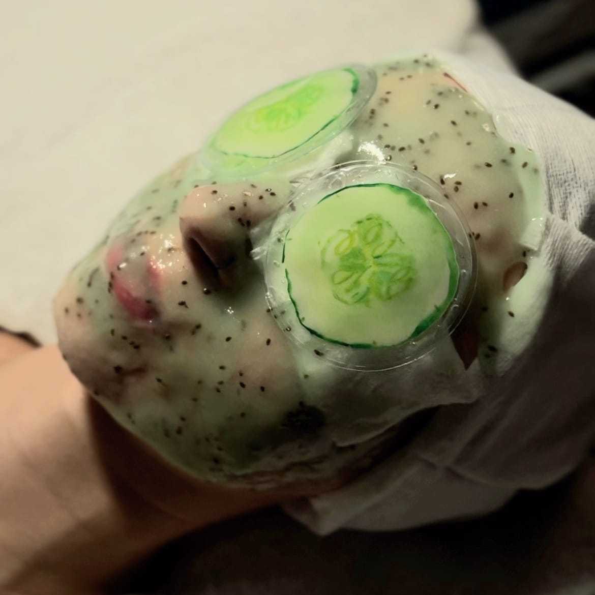 Person relaxing with a facial mask and cucumber slices on eyes at a spa.